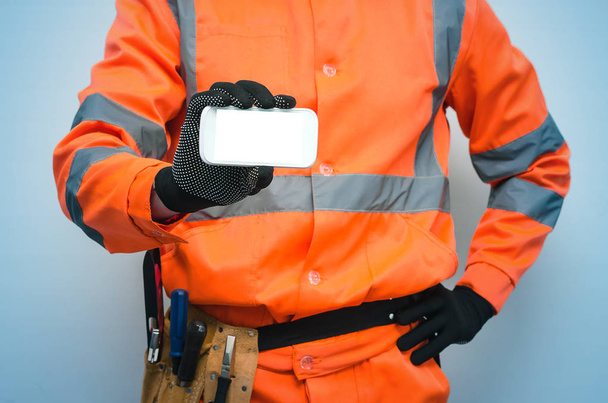 Builder worker is holding in hand a blank screen mobile phone. Call to a repair man concept. Contact us. - Foto, imagen
