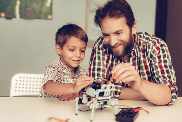 Bearded Father and Son Constructing Robot at Home. Young Boy in Shirt. Indoor Joy. Modern Hobby Concept. Modern Technology. Robot Engineering Concept. Bearded Young Man. Innovation for Fun. - Foto, imagen