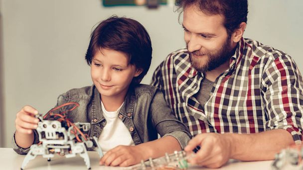 Bearded Father and Son Constructing Robot at Home. Young Boy in Shirt. Indoor Joy. Modern Hobby Concept. Modern Technology. Robot Engineering Concept. Bearded Young Man. Innovation for Fun. - Photo, image
