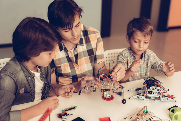 Teenager and Two Boys Constructing Robot at Home. Young Boy in Shirt. Indoor Joy. Modern Hobby Concept. Modern Technology. Robot Engineering Concept. Teenager with Robor. Innovation for Fun. - Foto, imagen