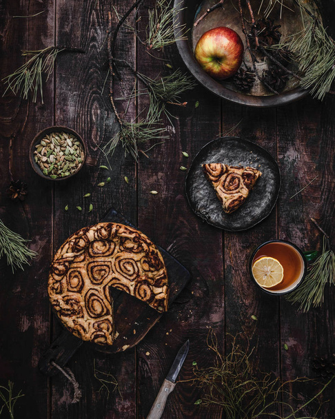 Top view of cinnamon rolled cake on rustic wooden background with spruce branches - Foto, Imagem