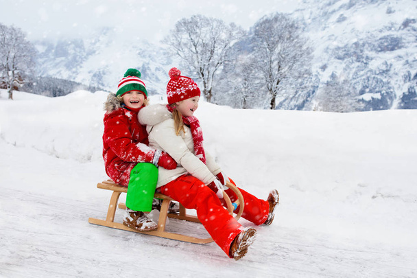 幼い女の子と男の子がそりに乗るのを楽しんでいます。子供のそり。幼児はそりに乗っている。子供たちは雪の中屋外で遊ぶ。冬のスノーパークで子供たちがそります。家族のための屋外の楽しみクリスマス休暇. - 写真・画像