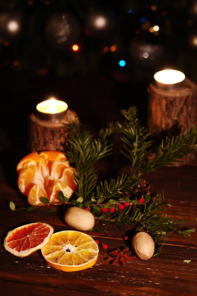 Winter festive dark still life. Candles, tangerines nuts on the background of sparkling lights. - Photo, Image
