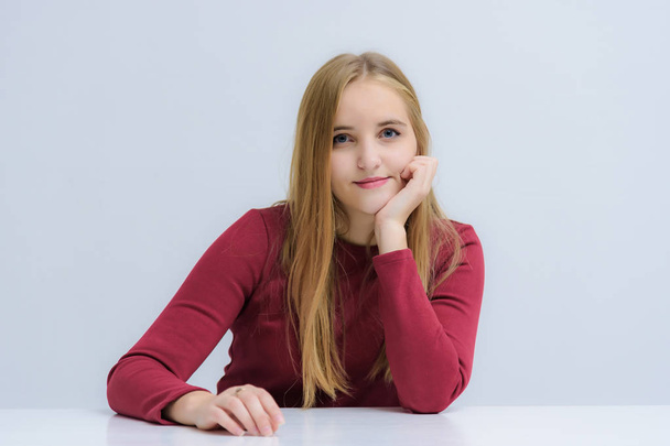 Concept portrait of a beautiful happy blonde girl on a white background smiling, talking with emotions while sitting at the table. She stands directly in front of the camera in various poses. - Foto, Imagem