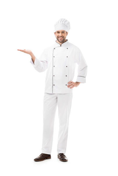 Ganzkörperansicht des jungen Kochs, der Kopierraum zeigt und isoliert auf Weiß in die Kamera lächelt - Foto, Bild
