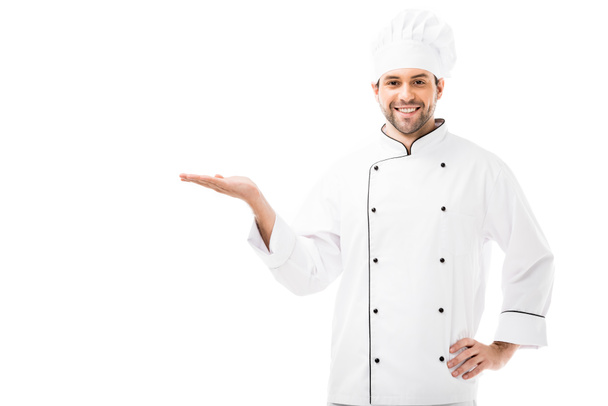 handsome young chef showing copy space and smiling at camera isolated on white - Foto, Imagem