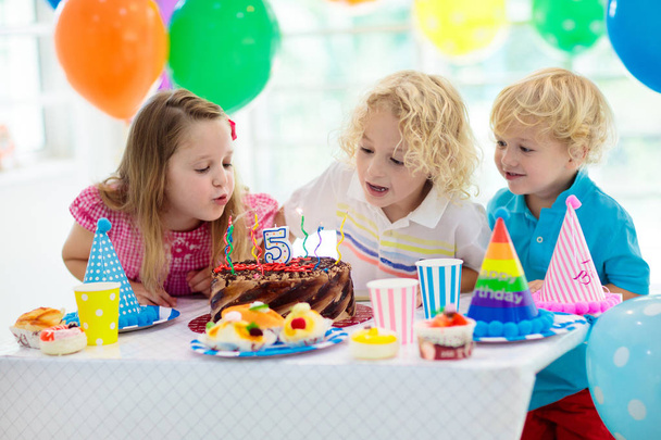 子供の誕生日パーティー。カラフルなケーキの上のろうそくを吹きの子。虹旗バナー、風船で飾られた家。ファーム動物のテーマにお祝いします。小さな少年の祝う誕生日。パーティー フード. - 写真・画像
