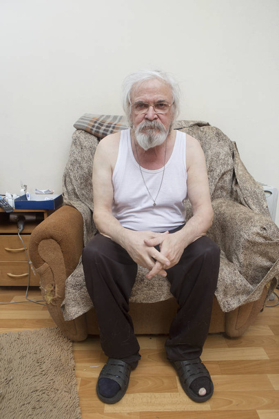 Um velho e solitário pobre homem doente, sofrendo de doença ocular com catarata e glaucoma, senta-se em uma cadeira sozinho
. - Foto, Imagem