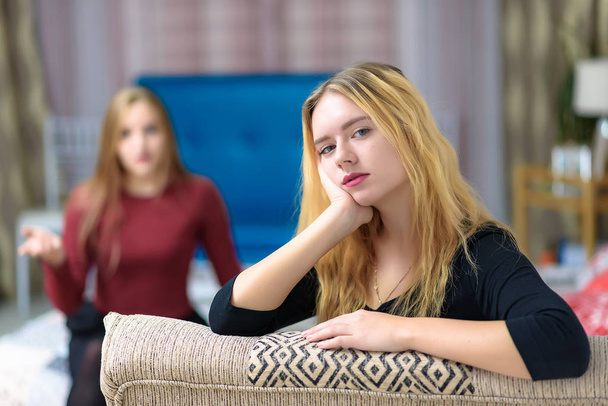 The concept of family problems a couple of beautiful young disgruntled lesbian girls are talking in a room sitting on a sofa. They are right in front of the camera and look unhappy. - Φωτογραφία, εικόνα