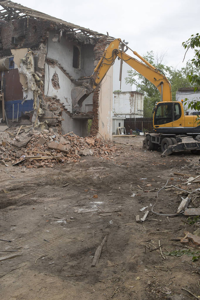 Разрушение стен старого здания и очистка строительного мусора ведром экскаватора. - Фото, изображение