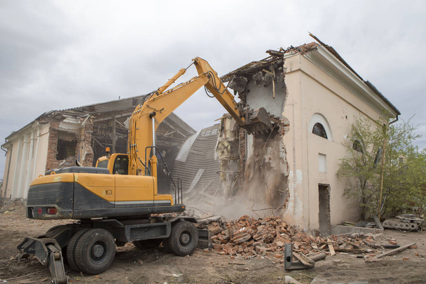A destruição das paredes do antigo edifício e a limpeza de detritos de construção com um balde de uma escavadeira. - Foto, Imagem
