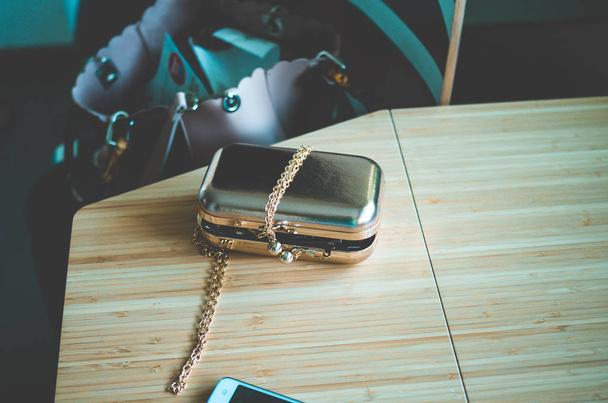 Embrague dorado como bolso de objeto de moda con teléfono móvil y mesa de bambú y bolso en el fondo en un aspecto retro fresco
 - Foto, imagen