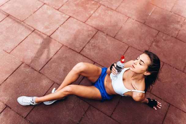 Cute sporty girl relaxing after outdoor training with bottle of water in hands. - Fotoğraf, Görsel