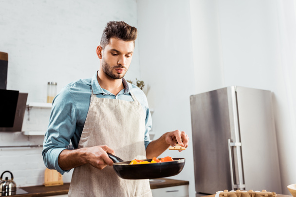 handsome young man in apron holding frying pan with vegetables - Foto, Bild
