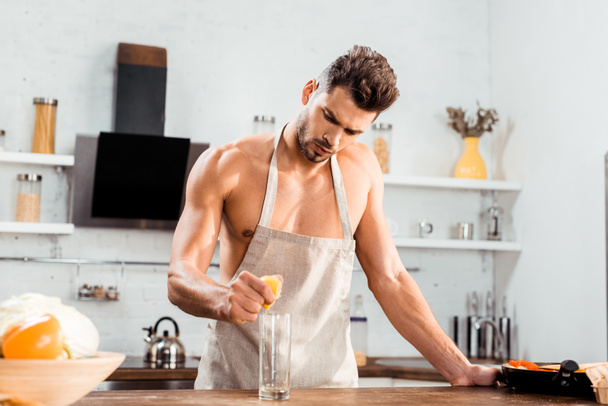 sexy young man in apron squeezing lemon in glass - Foto, Imagen