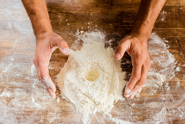 vista parcial de las manos masculinas y harina en la mesa de la cocina
 - Foto, Imagen