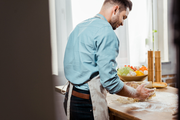 back view of young man in apron preparing dough in kitchen - Zdjęcie, obraz
