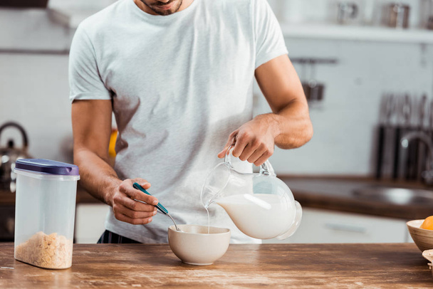 cropped shot of man pouring milk into bowl with corn flakes for breakfast - Fotó, kép