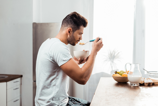 Widok z boku z młodego człowieka w piżamie jeść płatki na śniadanie w domu - Zdjęcie, obraz