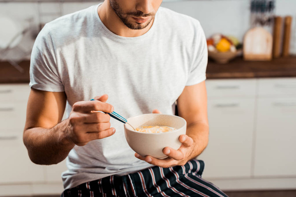 cropped shot of young man in pajamas eating cereals for breakfast at home - Foto, imagen