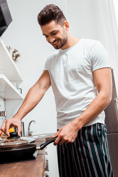 vista de ángulo bajo del joven sonriente en pijama cocinando tortilla en sartén
 - Foto, Imagen