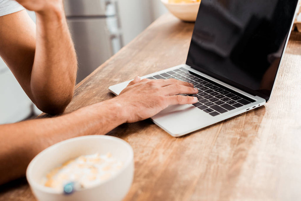cropped shot of man using laptop with blank screen on kitchen table at morning - Photo, image
