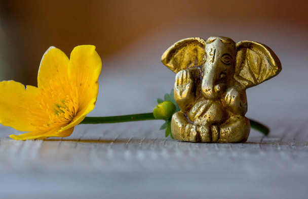 Ganesha Figur mit leuchtend gelben Blüten Nahaufnahme. schöne Ganesh-Statue mit offener Palme und blühender Blume auf Holzbrett. asiatisches Religionskonzept. religiöse Dekoration. Indischer Lord. Friedenskonzept. - Foto, Bild
