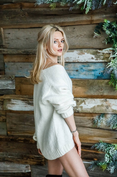 Studio portrait of beauty blond woman wearing white sweater. Female model standing on wooden wall background - Foto, Bild