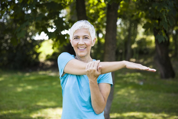 Mujer mayor haciendo ejercicio tretching brazo en el parque en el día de verano
 - Foto, Imagen