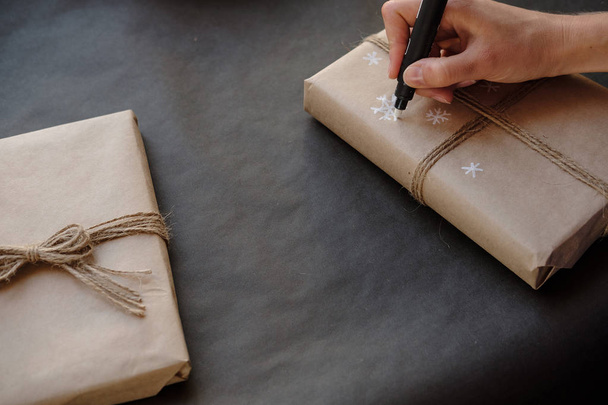 Vrouw sneeuwvlokken puttend uit papier pakket Christmas box cadeau op zwarte achtergrond. Vrouwelijke handen schilderen op cadeaus voor wintervakantie. Kerstmis, Nieuwjaar, winkelen, voorbereiding op vakantie concept - Foto, afbeelding