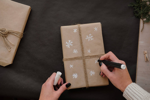 Woman drawing Snowflakes on paper package Christmas box Gift on black background. Female hands painting on Presents for winter Holidays. Christmas, New Year, shopping, preparation on Holidays concept - Photo, Image