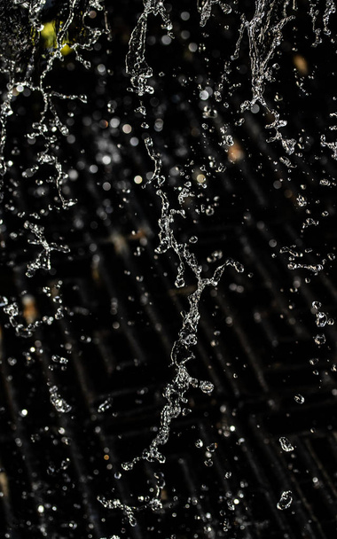 Water splash in dark with a drops of water flying, defocused bokeh. - Photo, Image