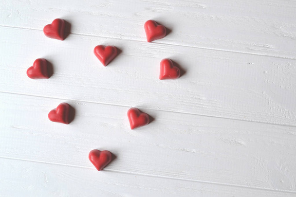 Rode snoepjes in de vorm van hart en rode kaarsen op de witte houten tafel. Achtergrond voor de wenskaart op Valentijnsdag met plaats voor tekst. - Foto, afbeelding