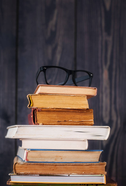 Stack of hardback books with reading glasses on dark wooden background. Back to school. Copy space. - Foto, Imagem