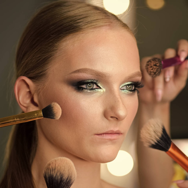 Girl getting powder on skin with makeup brushes. Girl with getting makeup on face. - Photo, Image
