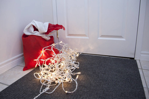  Een rode zak met cadeautjes en een wirwar van kerstverlichting door de deur van een huis  - Foto, afbeelding