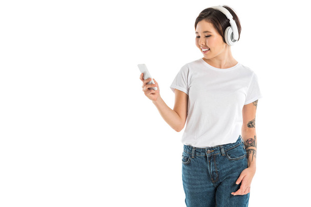 attractive young woman wearing headphones, listening music and using smartphone isolated on white - Foto, afbeelding