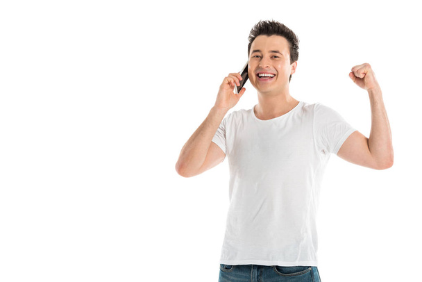 excited handsome man talking on smartphone and cheering isolated on white - Foto, imagen