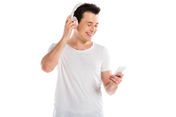 Lächelnder gutaussehender Mann mit Kopfhörern, Smartphone isoliert auf weiß - Foto, Bild