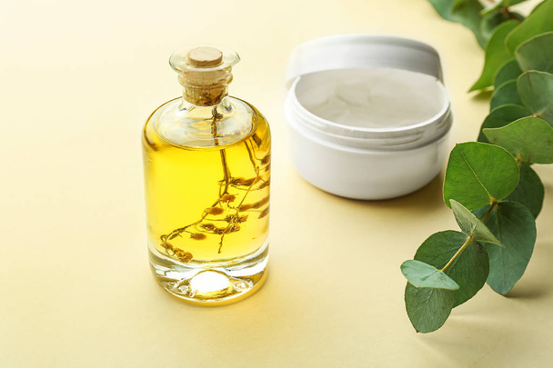 Cream and bottle of eucalyptus essential oil on color background - Fotoğraf, Görsel