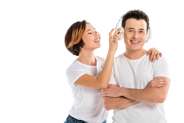 ευτυχισμένη σύζυγος βάζοντας τα ακουστικά σε χαμογελαστός ο σύζυγός που απομονώνονται σε λευκό - Φωτογραφία, εικόνα