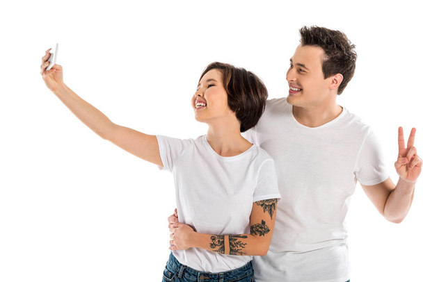 χαμογελαστά ζευγάρι λήψη selfie σε smartphone και δείχνει σημάδι ειρήνης που απομονώνονται σε λευκό - Φωτογραφία, εικόνα