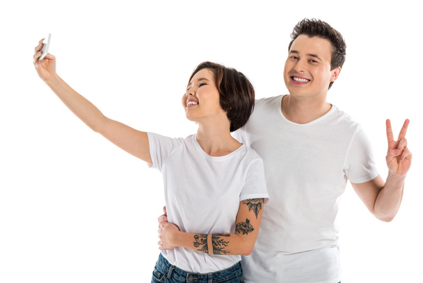 happy couple taking selfie on smartphone and showing peace sign isolated on white - Fotoğraf, Görsel