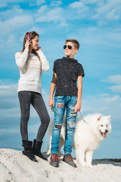 Happy 11 letý chlapec svouvlastní psí plemeno samojed u pobřeží proti modré obloze zblízka. Nejlepší odpočinek přátel a bavit se na dovolené, hrát v písku - Fotografie, Obrázek