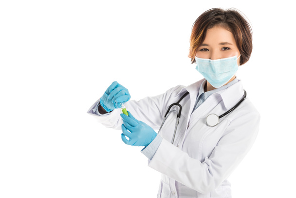 female doctor with stethoscope and medical mask holding ampule and looking at camera isolated on white - Fotó, kép