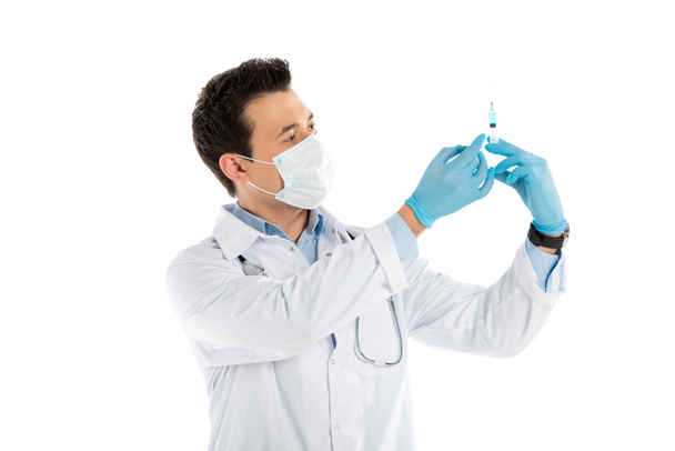 concentrated male doctor in rubber gloves and mask holding syringe isolated on white - Photo, Image