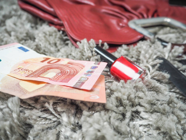 Δύο σημειώσεις δέκα ευρώ, που βρίσκεται δίπλα σε μια κόκκινη γυναικεία τσάντα και κόκκινο βερνίκι νυχιών διάσπαρτα σε μια γκρίζα τάπητα βελούδου - Φωτογραφία, εικόνα