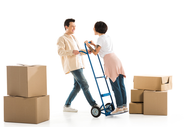 husband holding wife on hand truck with cardboard boxes on background, moving to new house concept - Φωτογραφία, εικόνα