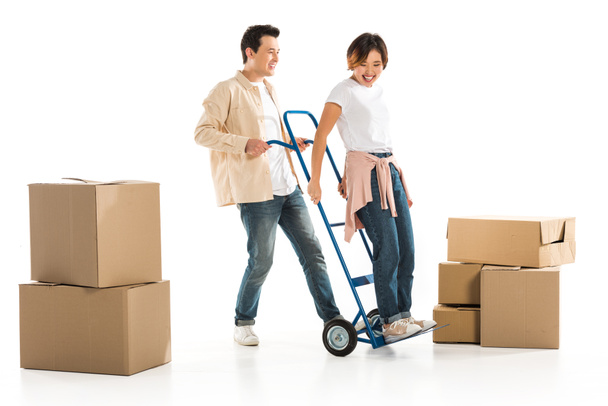husband giving ride wife on hand truck with cardboard boxes on background, moving to new house concept - Photo, Image