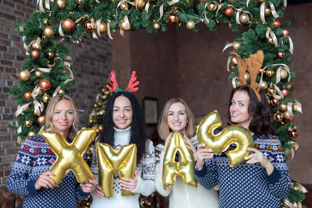 Mujeres jóvenes sosteniendo la palabra Navidad hecha de globos de oro
 - Foto, Imagen